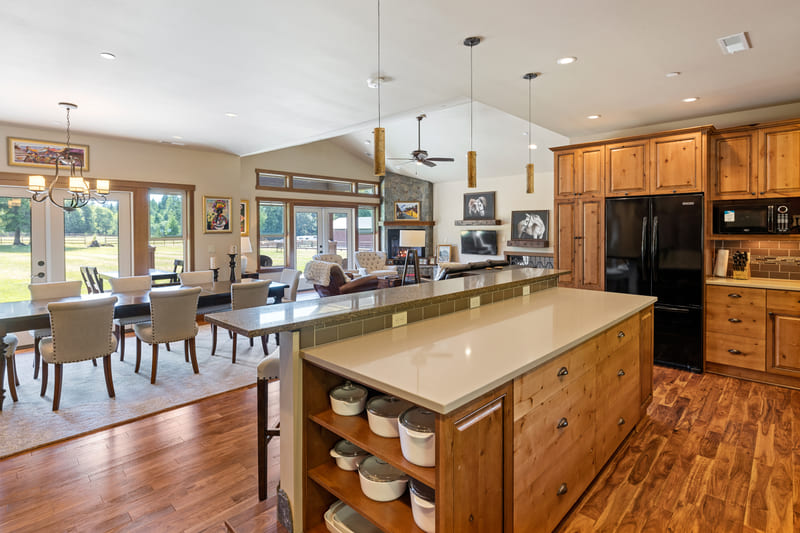 Open kitchen with a quartz island, knotty wood cabinetry, and a tile backsplash, looking through to the dining area and living room.