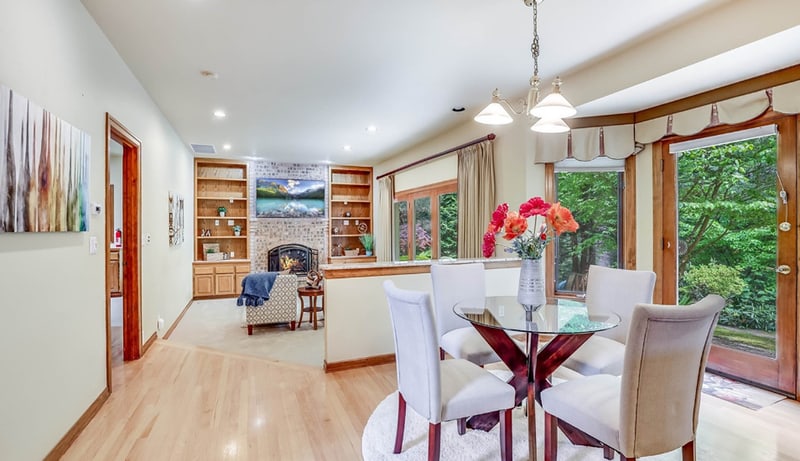 Dining area with a glass table and upholstered chairs, open to a living room with a fireplace and glazed doors to the garden.