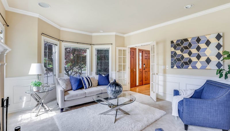 Living room with a bay window and a sofa, looking through to the entry hall and the front door beyond glazed doors.