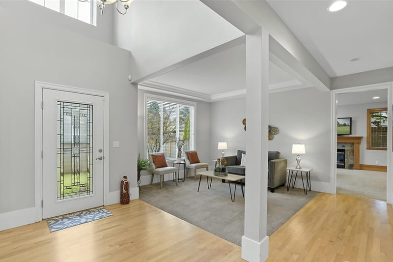 Entry hall with light hardwood floors looking into a sitting area with two armchairs, a sofa, and a large window.