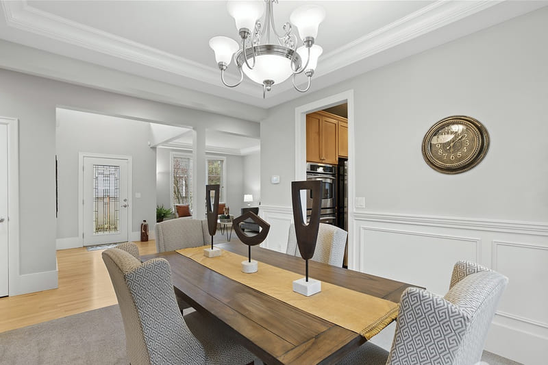Formal dining room with a wood table, patterned upholstered chairs, panelled wainscoting, and a tray ceiling with a chandelier.