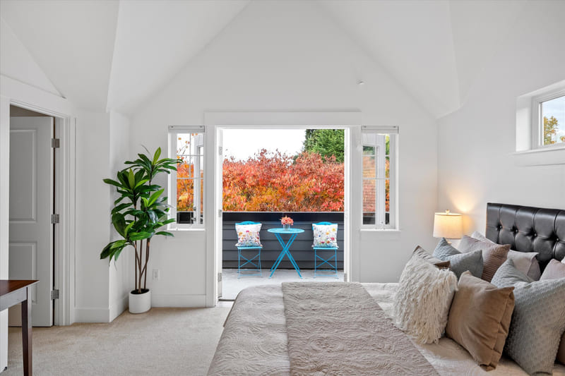 Bedroom with a vaulted ceiling, an upholstered headboard, and French doors opening to a small balcony with a bistro table.